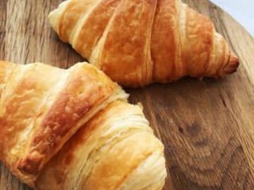 Two golden croissants on a wooden board.
