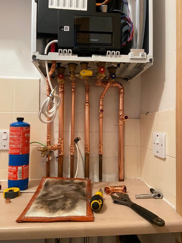 Copper pipes and plumbing tools under a boiler.