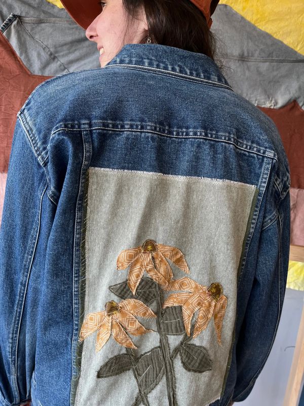 Denim jacket with a patch of three patterned flowers on the back.