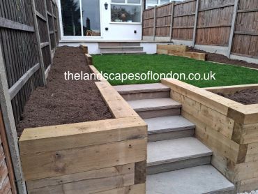 Newly built wooden garden retaining walls with steps and fresh soil beds.