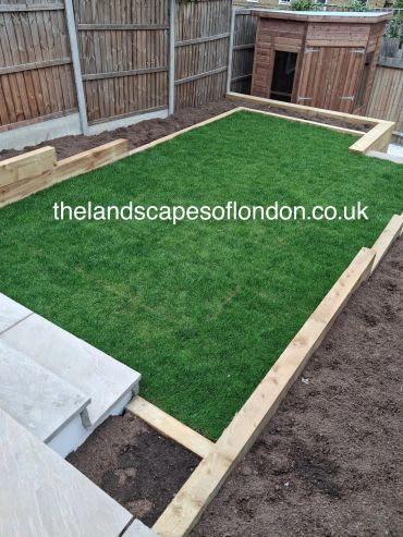 Newly installed artificial grass with wooden border in a backyard.