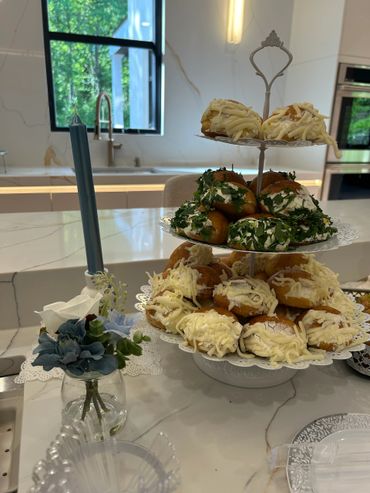 Two-tiered stand with frosted cupcakes on a marble table near a candle and flowers.