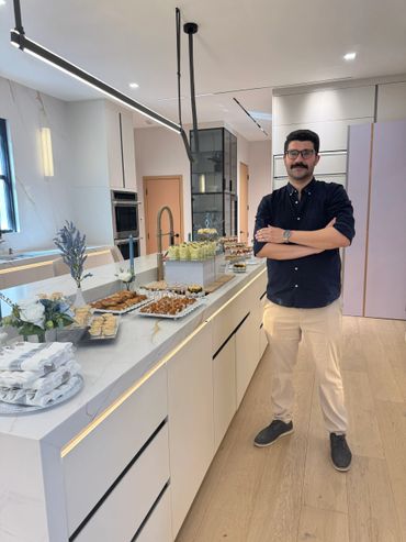 Man standing with arms crossed near a table with snacks and drinks in a modern kitchen.