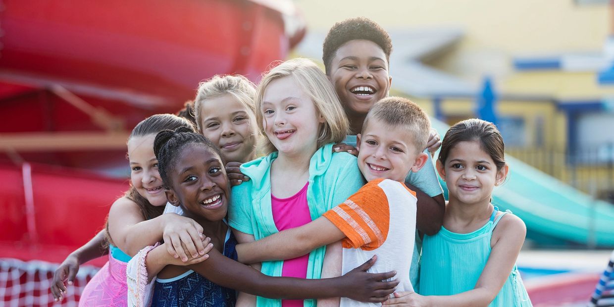 A diverse group of happy children hugging and smiling at an outdoor playground.