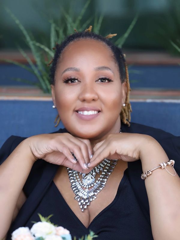 Smiling woman with layered necklace and bracelet rests chin on hands.