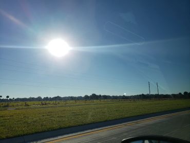 Bright sun over a grassy field beside a road.
