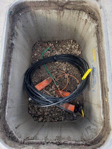 Open utility box with coiled black cables inside.