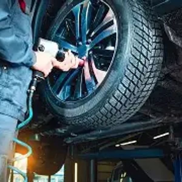 Mechanic using pneumatic tool to fix a car tire on a lift.