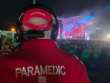 Paramedic monitoring a crowded outdoor event at night with colorful stage lights.