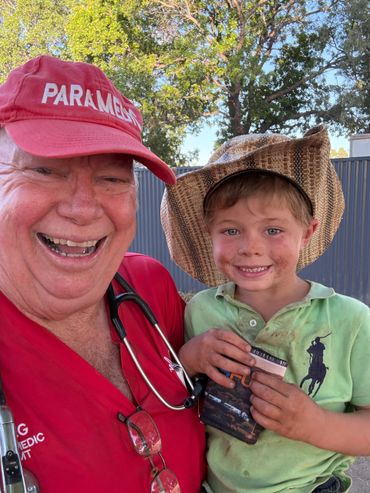 Smiling paramedic with a young boy wearing a cowboy hat outdoors.