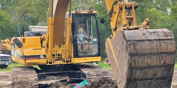 Child and adult inside a yellow excavator at a construction site.