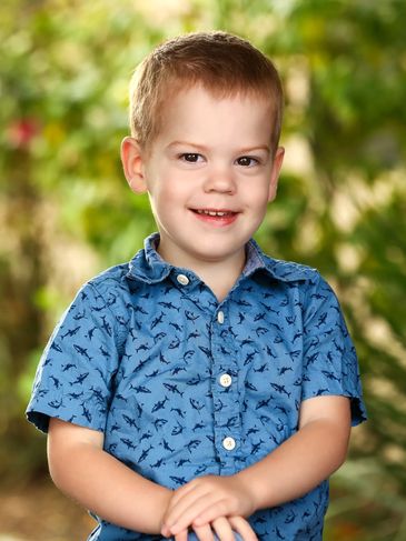 Smiling young boy in a blue shark-patterned shirt outdoors.