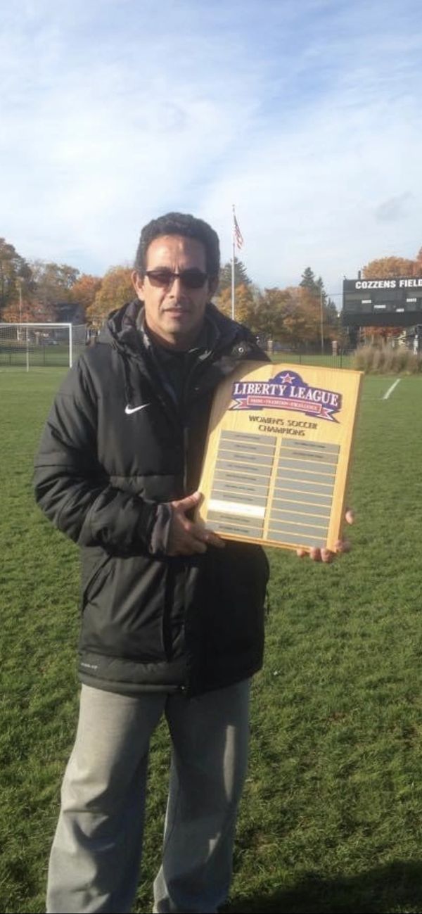 Man holding a Liberty League Women's Soccer Champions plaque on a soccer field.