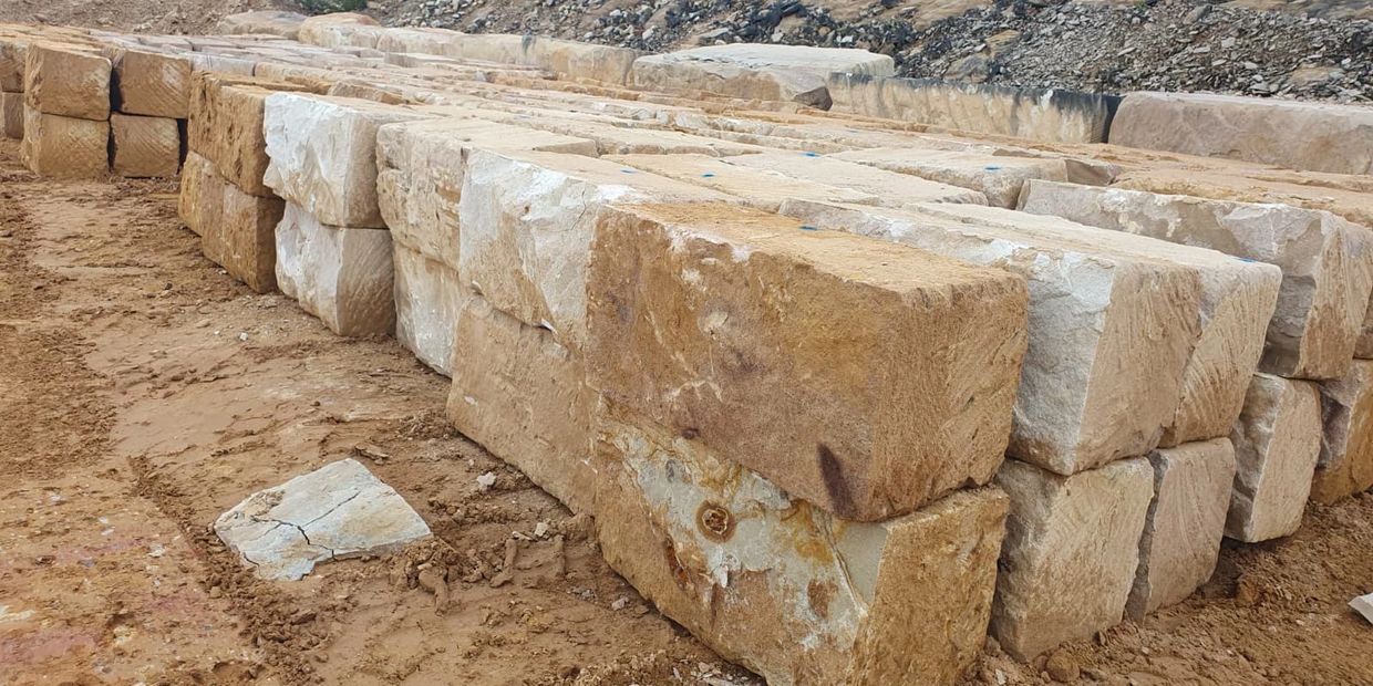 Stacks of large, rough-cut sandstone blocks on a dirt ground.