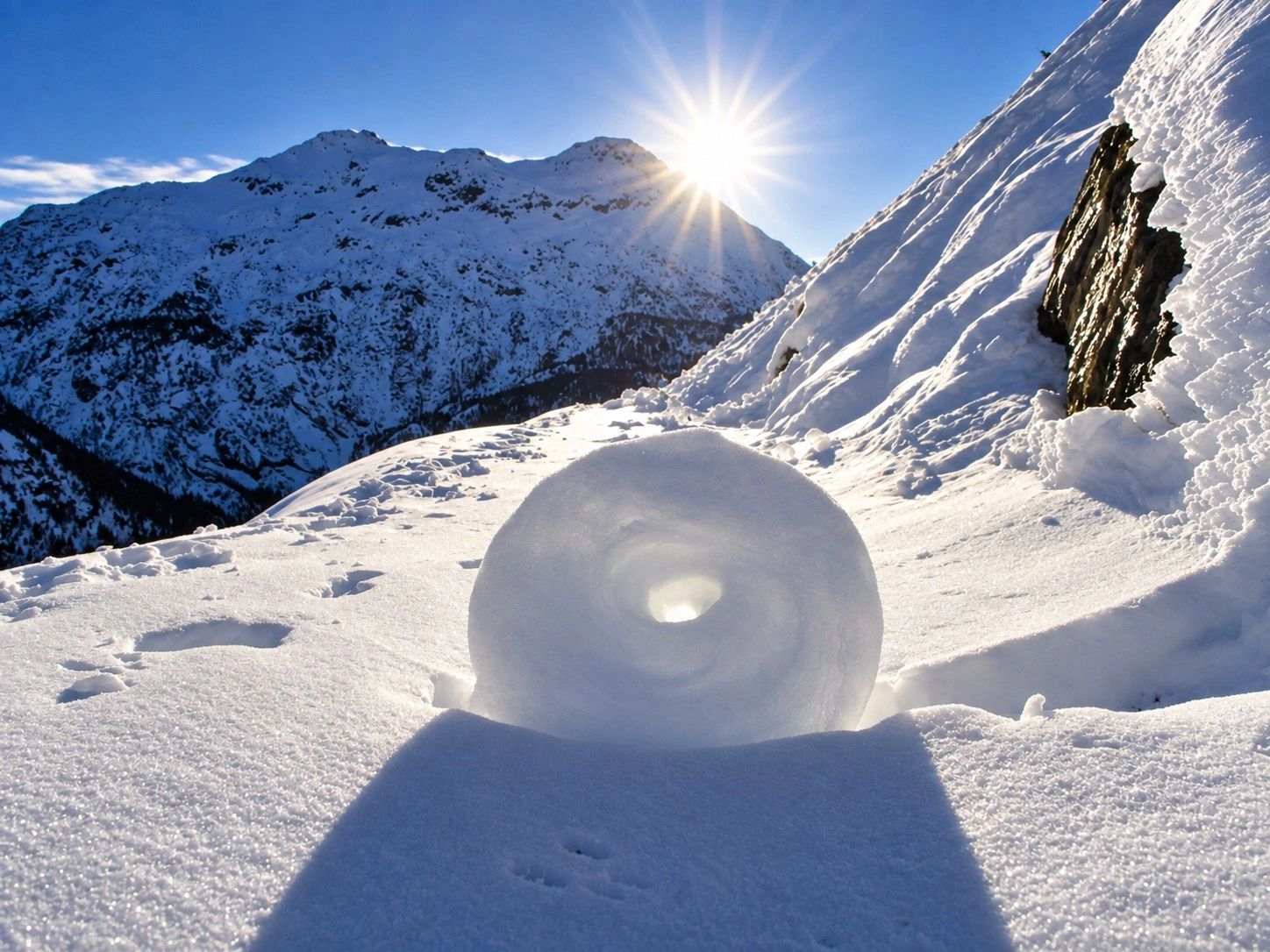 Paesaggio alpino invernale in Valtellina con montagne innevate e sole.