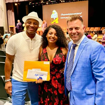 Three people smiling at a graduation event, one holding an envelope.
