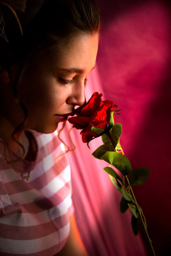 Woman smelling a red rose with a pink background.