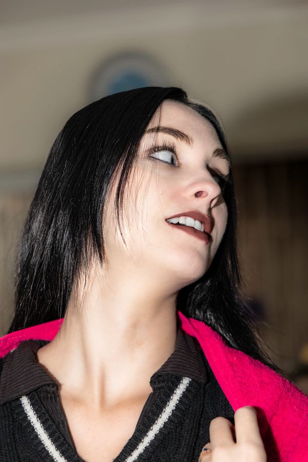 Young woman with long black hair looks to the side, wearing a black top and holding a red jacket.