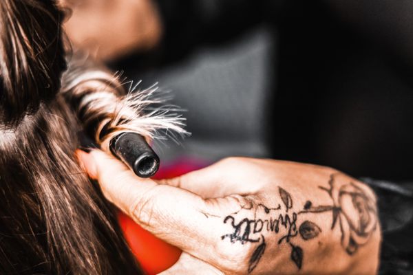 Close-up of a hand holding a curling iron near hair with tattooed fingers.