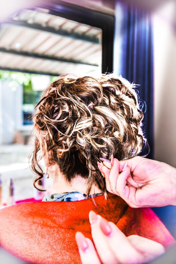 Person styling curly hair with manicured nails indoors.