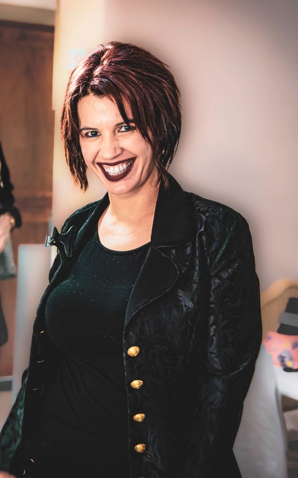 Woman with short red hair and dark lipstick smiling in a black outfit.