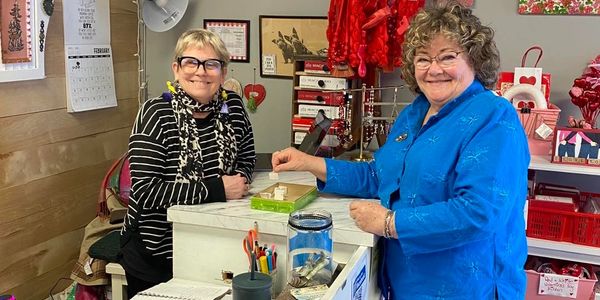 Two women smiling at a counter in a cozy shop with Valentine decorations.