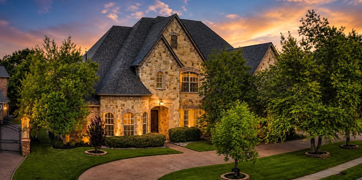 A large stone house with warm lighting at sunset and lush greenery.