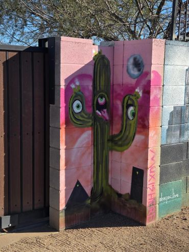 Colorful graffiti of a three-eyed cactus on a wall corner with a pink and orange background.