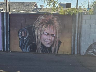 Mural of a character with wild hair holding a reflective orb on a brick wall.