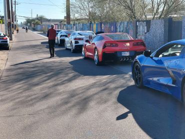 A lineup of sports cars parked along a sunny street with a person walking nearby.