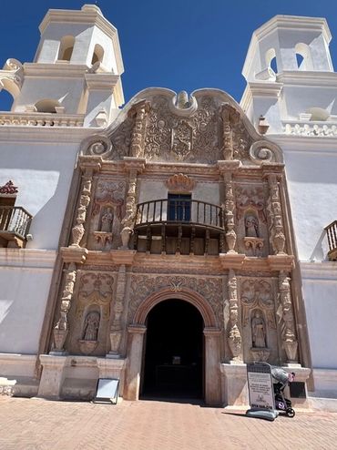 Historic ornate church facade with detailed carvings and twin bell towers against a clear blue sky.
