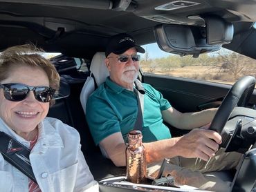 A smiling couple inside a car, with the man driving and the woman taking a selfie.
