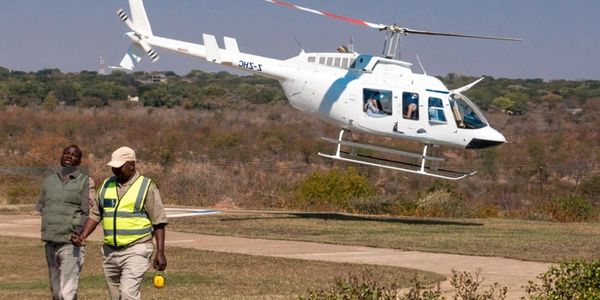A helicopter hovers near two men walking on a grass field.