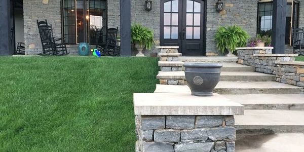 Stone steps and patio with rocking chairs in front of a house.