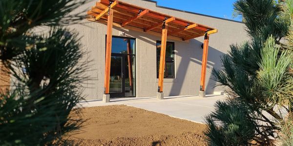 Modern building entrance with wooden pergola and concrete pathway.