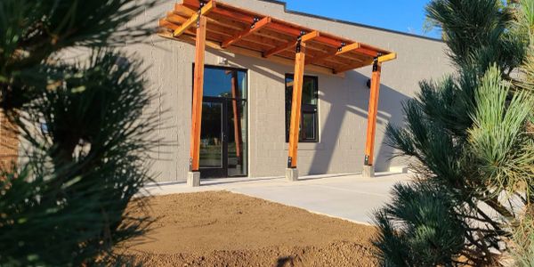 Modern building entrance with wooden pergola and concrete pathway.