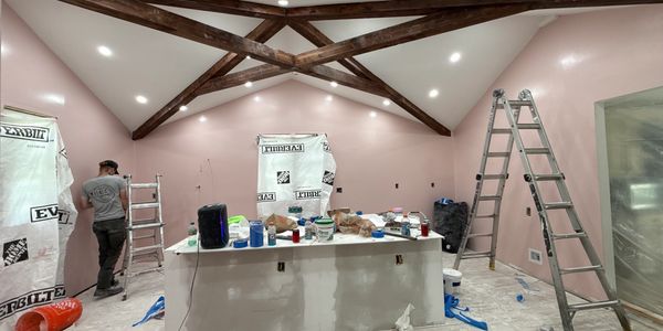 Interior room under renovation with exposed wooden beams and painting supplies.
