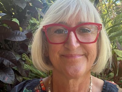 Smiling woman with white hair and red glasses outdoors.