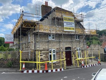 Stone house surrounded by scaffolding with roofing signs.