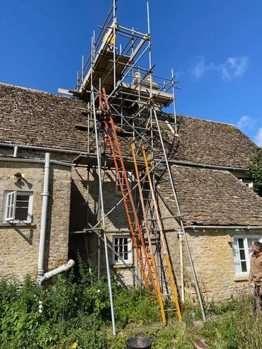 Scaffolding set up against a stone house under a clear blue sky.