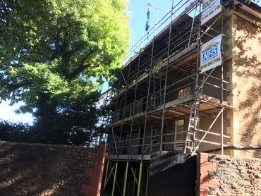 Building under renovation with scaffolding and a large tree nearby.