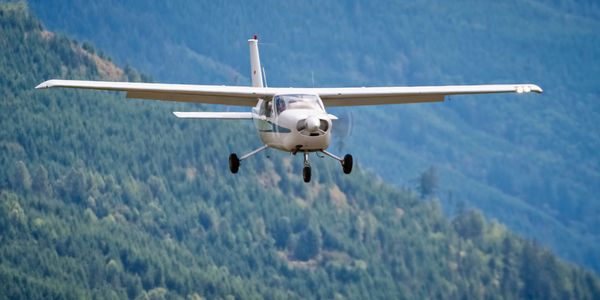 Small airplane flying low over forested mountains.