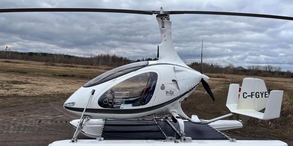 A white autogyro helicopter parked on a cloudy day in an open field.
