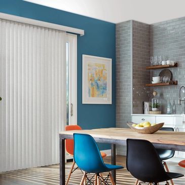 Modern dining area with colorful chairs and wooden table beside kitchen and sliding door covered with vertical blinds.