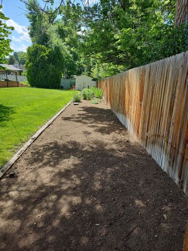 Freshly tilled garden bed beside a wooden fence on a sunny day.