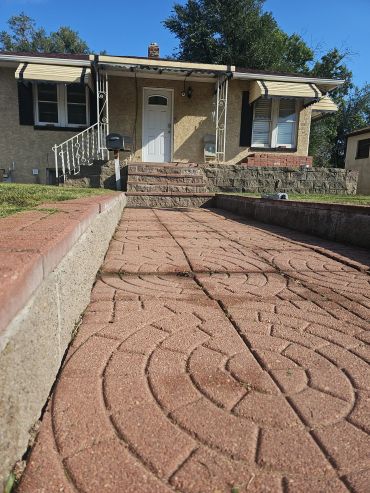 Decorative paved walkway leading to a house entrance with steps and a small porch.