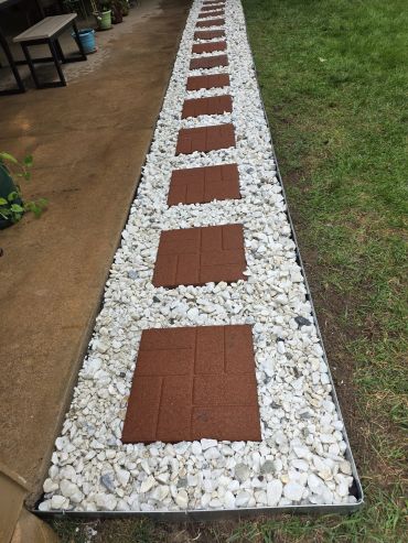 Pathway with red square tiles embedded in white stones runs alongside grass and concrete.