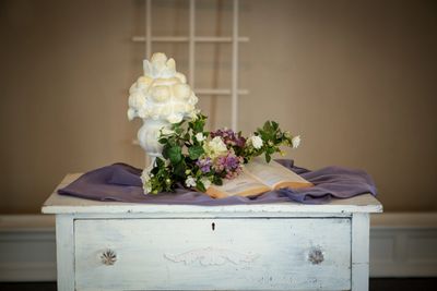 A white bust, flowers, and an open book on a vintage white table.