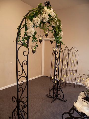 Decorative black metal arch with white flowers and hanging glass candles.