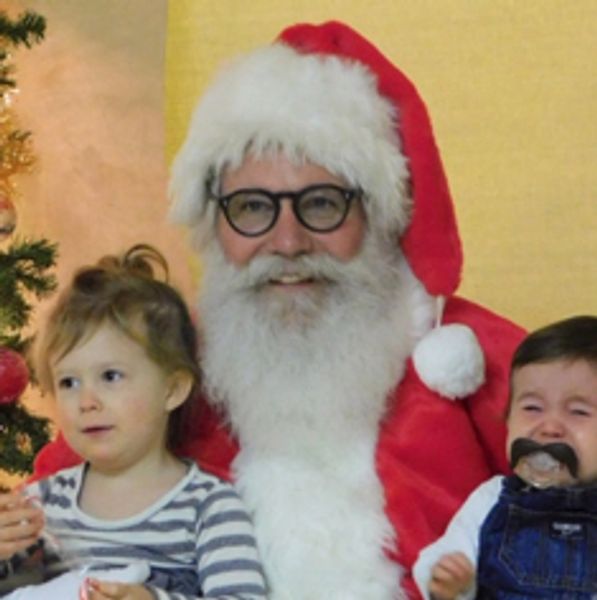 Santa Claus with two young children, one happy and one crying.